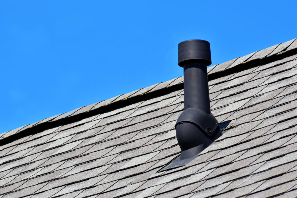 Black air ventilation chimney on grey shingles roof of residental house
