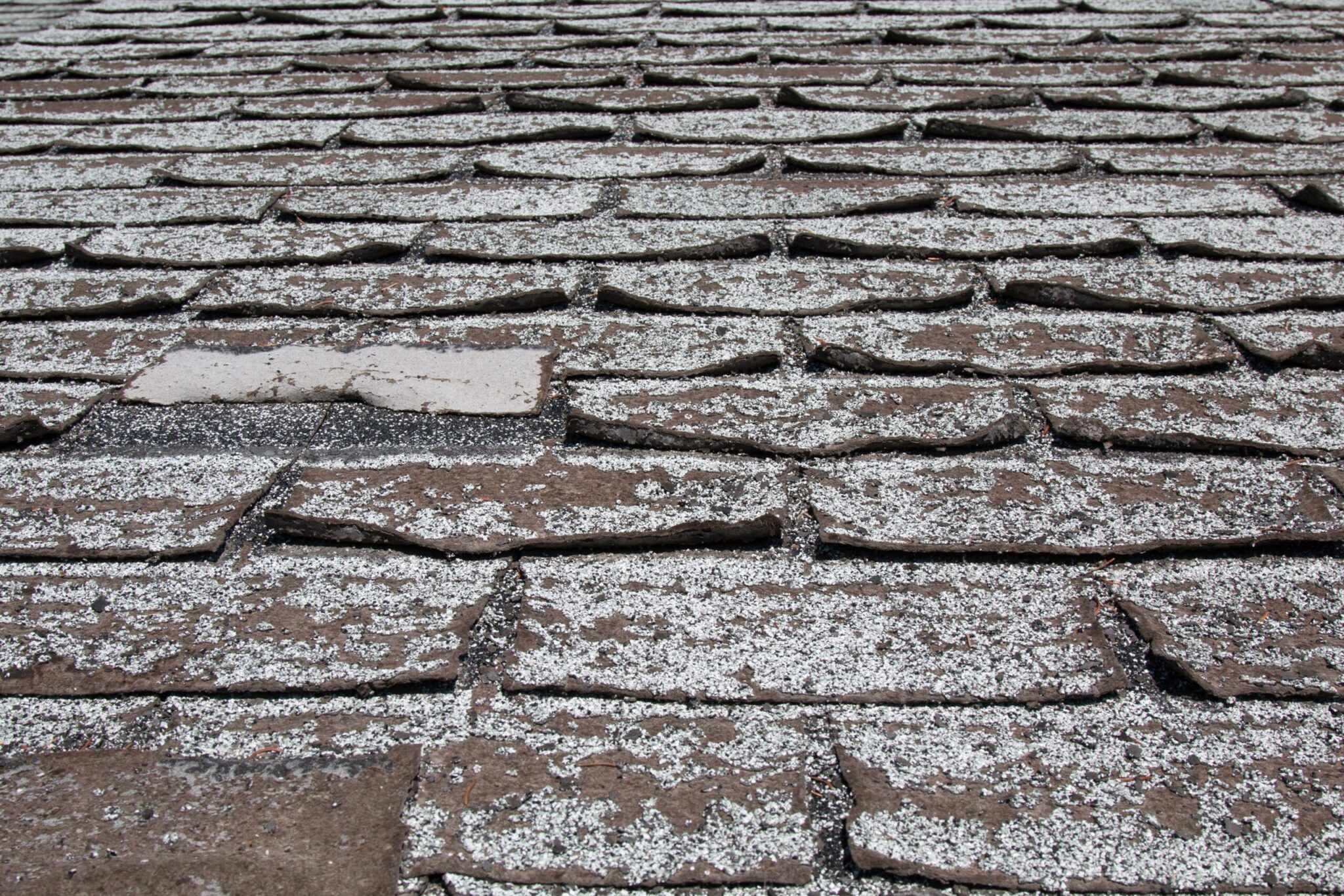 Old worn out asphalt shingles on the roof of a residential home.